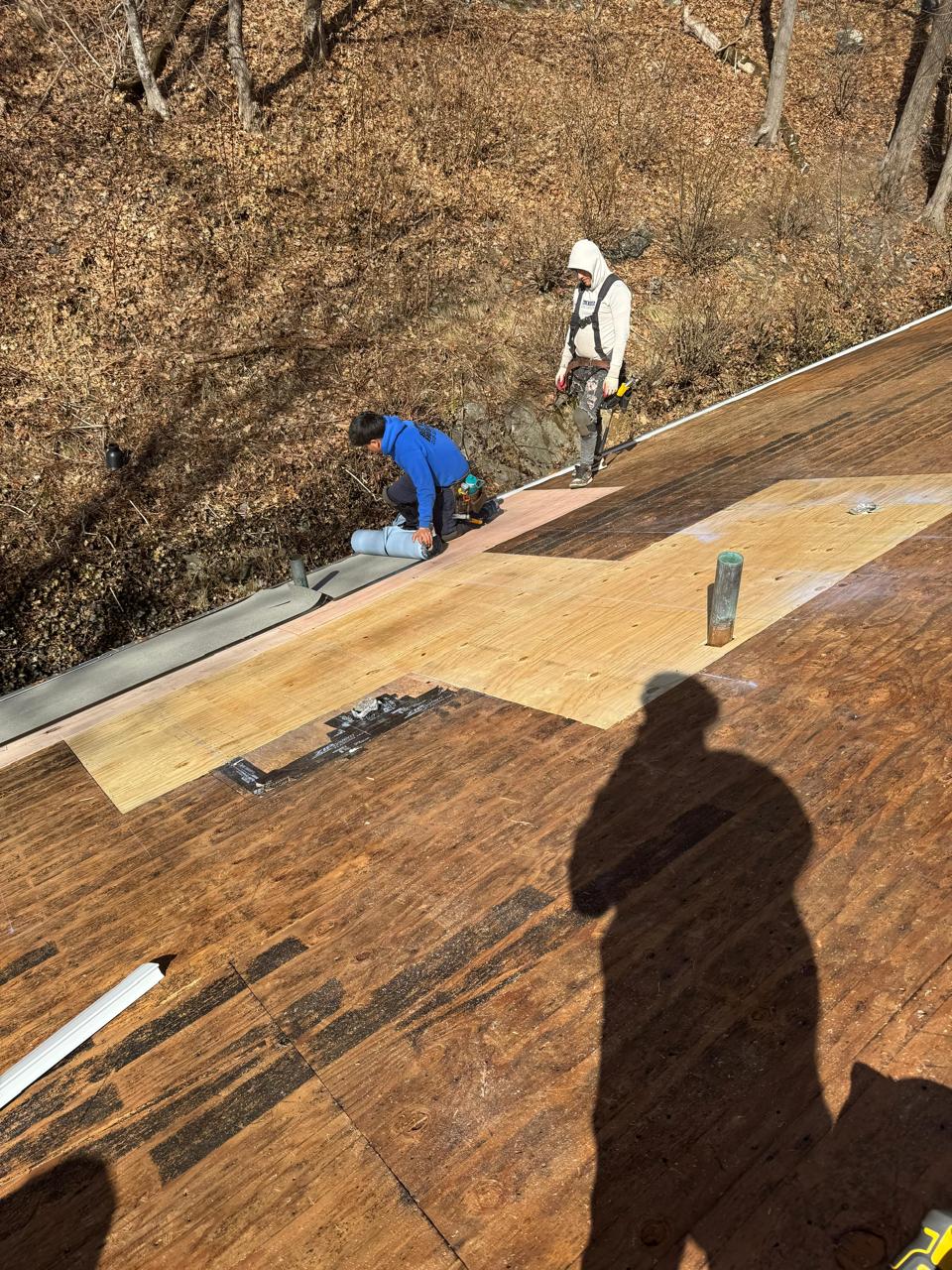Worker on a bare plywood roof deck during a tear-off